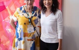 Two guests pose together, smiling in front of a pink and orange abstract painting.