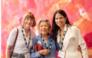 Three women pose together, smiling in front of a vivid abstract painting at Lonsdale Gallery.