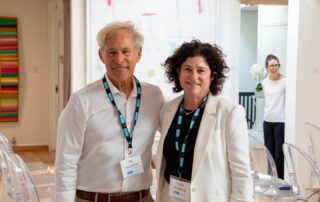 . Two smiling guests wearing lanyards pose together at the art event reception.