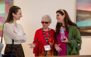 Three women enjoying conversation next to the display tables at the Artists in the Spotlight gallery.