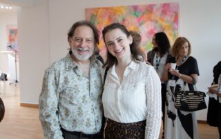 Two young guests smiling together inside the bright gallery at Baycrest’s art event.