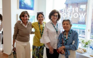 smiling women pose together, wearing name badges, at the art showcase event.
