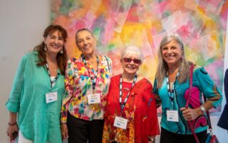 Four women in colourful outfits smiling together at Baycrest’s Lonsdale Gallery talk and tour.