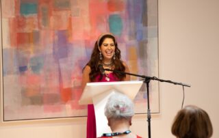 Speaker presenting at the podium with a vibrant abstract artwork in the background.