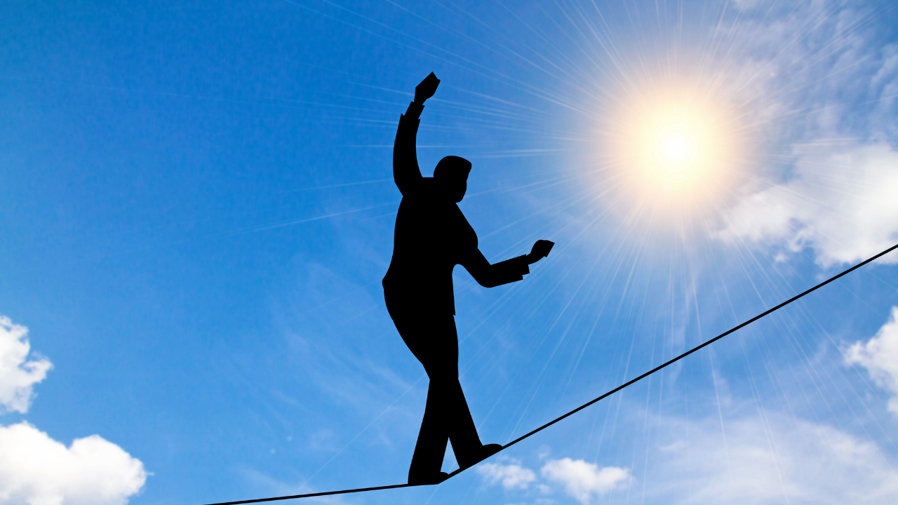 A person balancing on a tightwire with a blue sky with clouds behind them