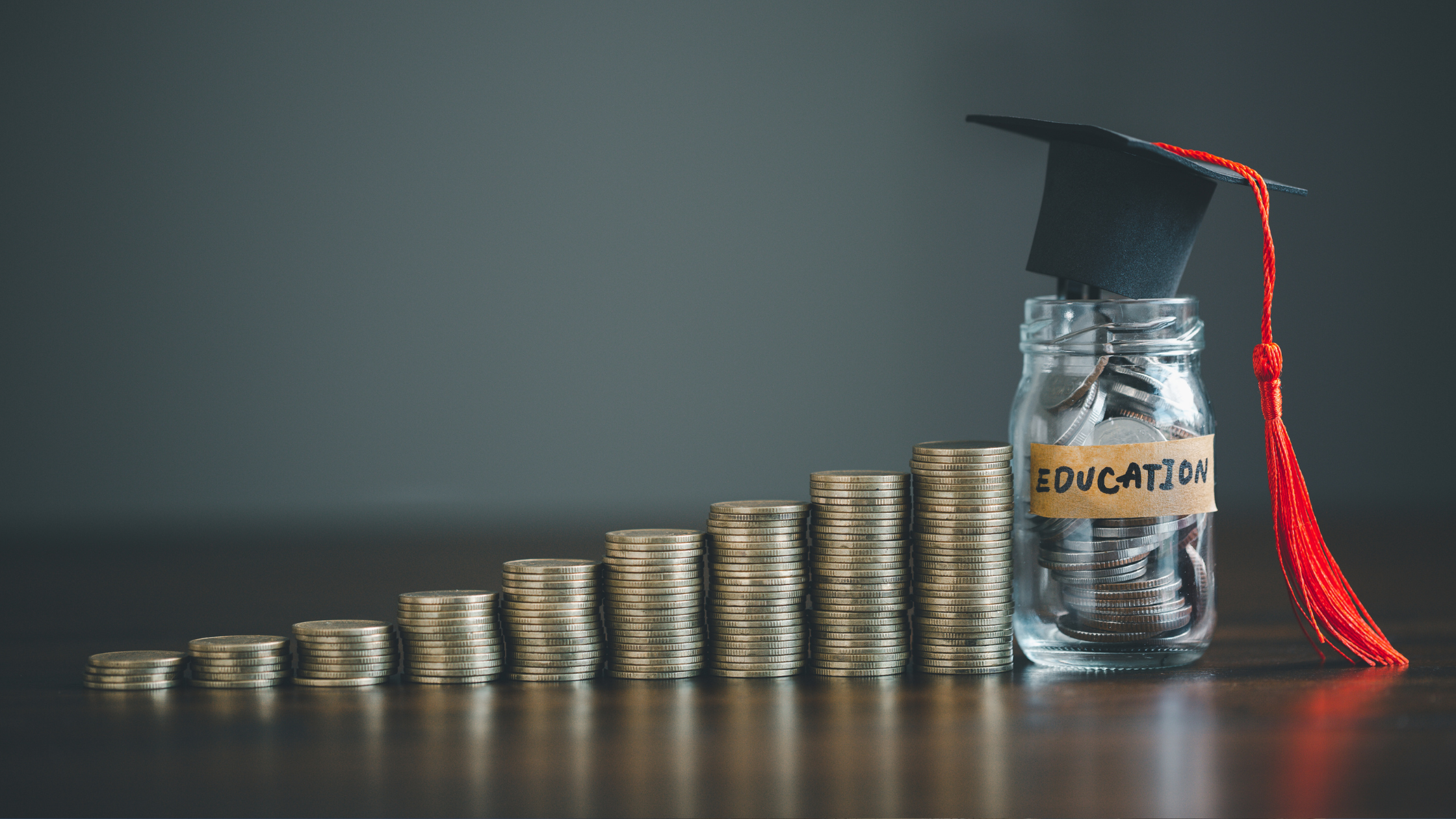 A stack of coins getting progressively larger leading to a jar of money with a graduation cap on top.