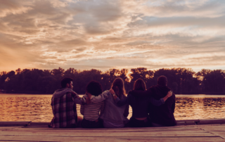 A group of close friends witting on a dock with sunset behind them, showing how caregivers can maintain friendships
