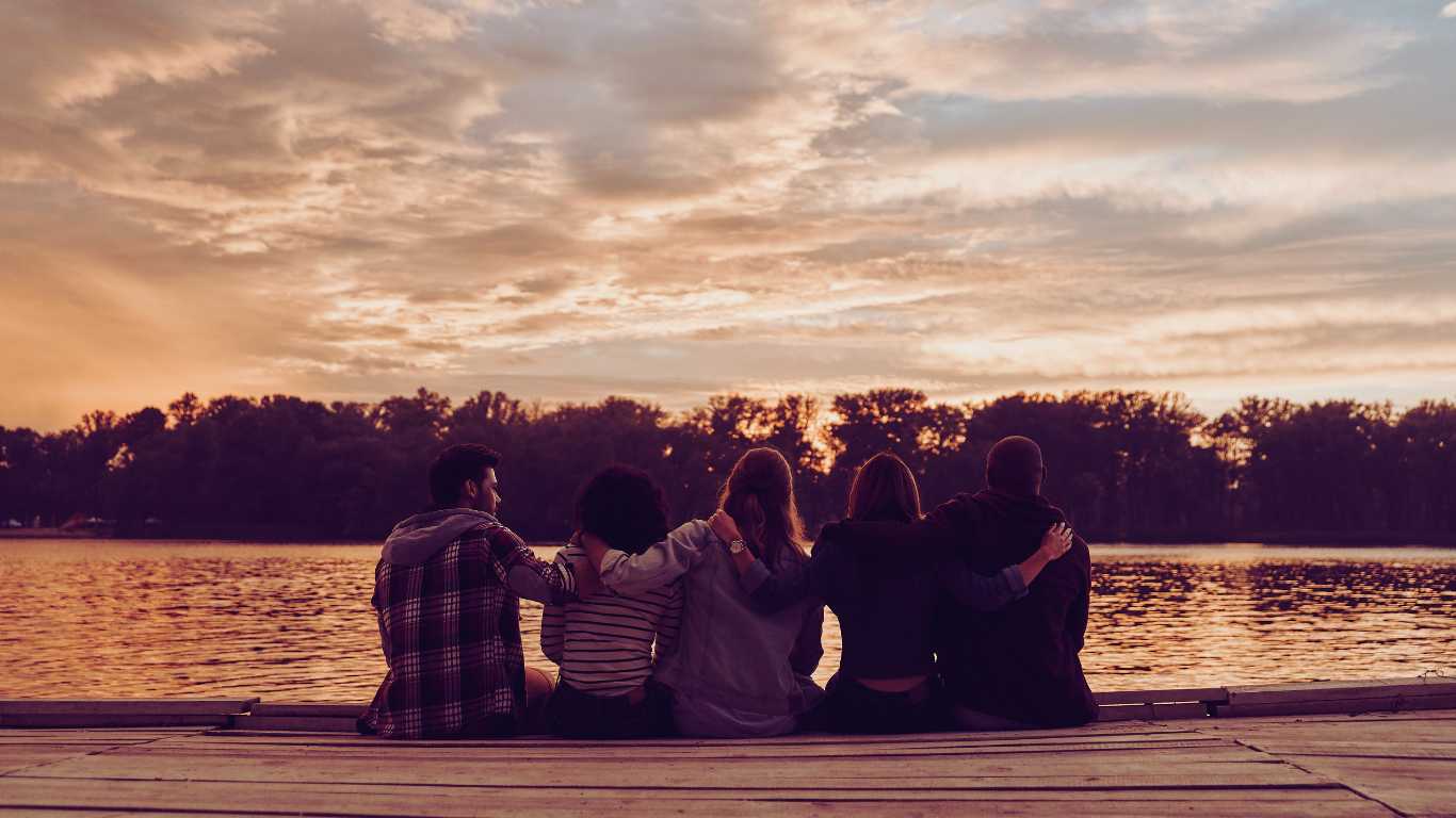 A group of close friends witting on a dock with sunset behind them, showing how caregivers can maintain friendships