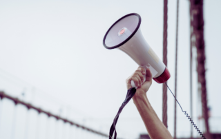 An advocate for dementia care holding a white megaphone against a white wall.