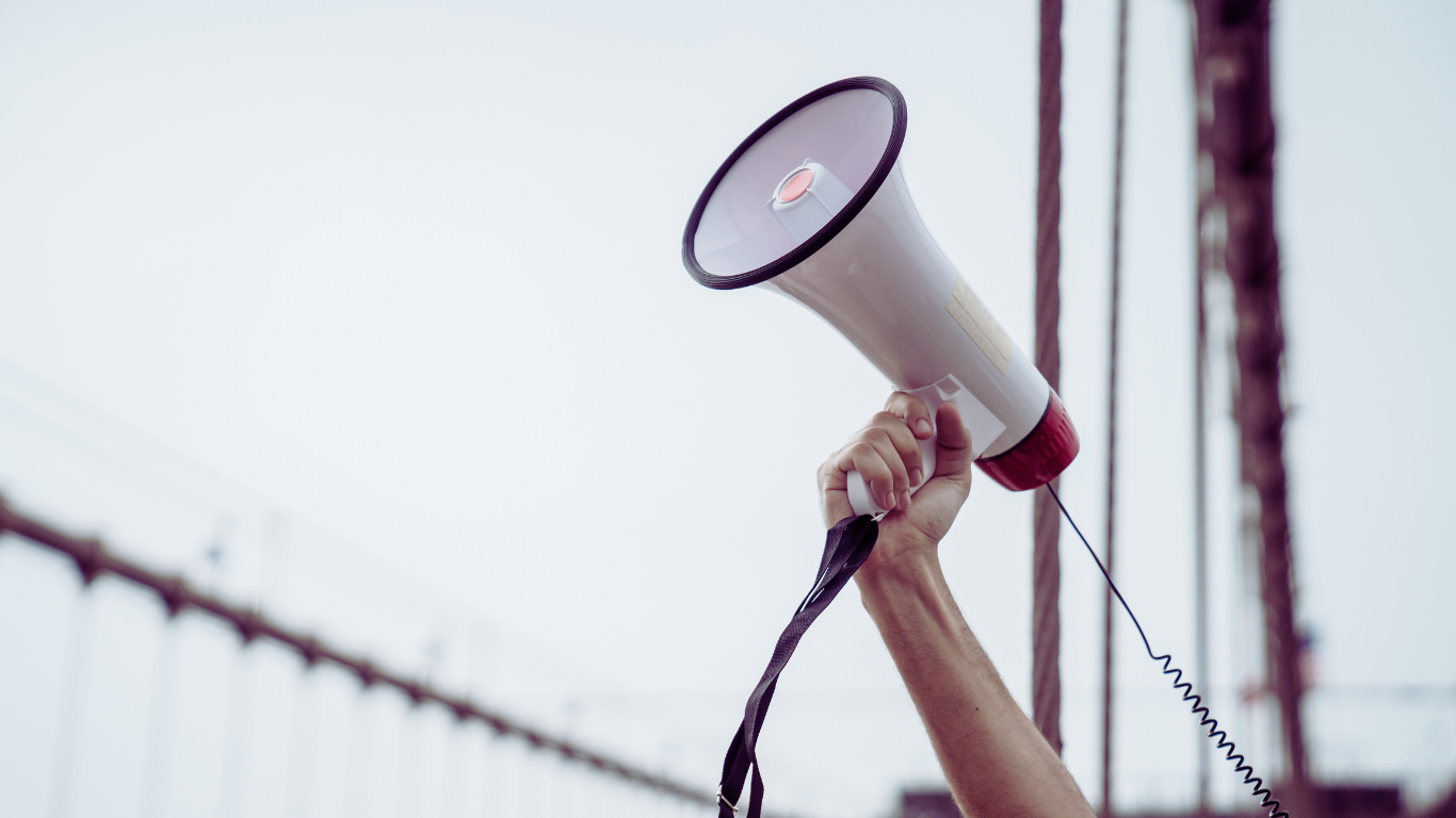 An advocate for dementia care holding a white megaphone against a white wall.