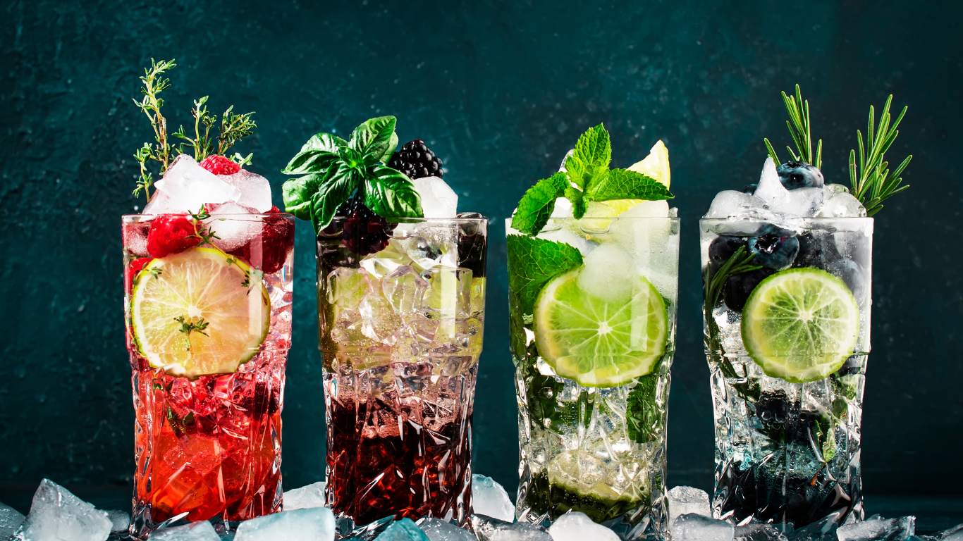 A collection of refreshing looking mocktails lined up on a bar with a forest green backround