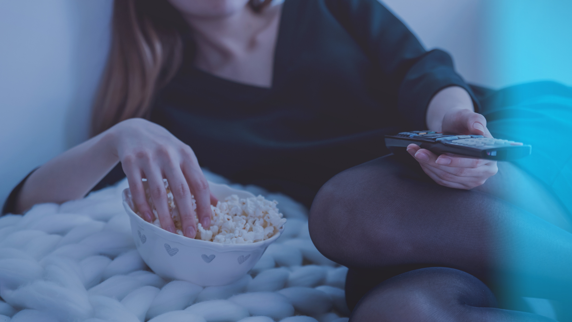 Woman is watching TV in bed eating popcorn