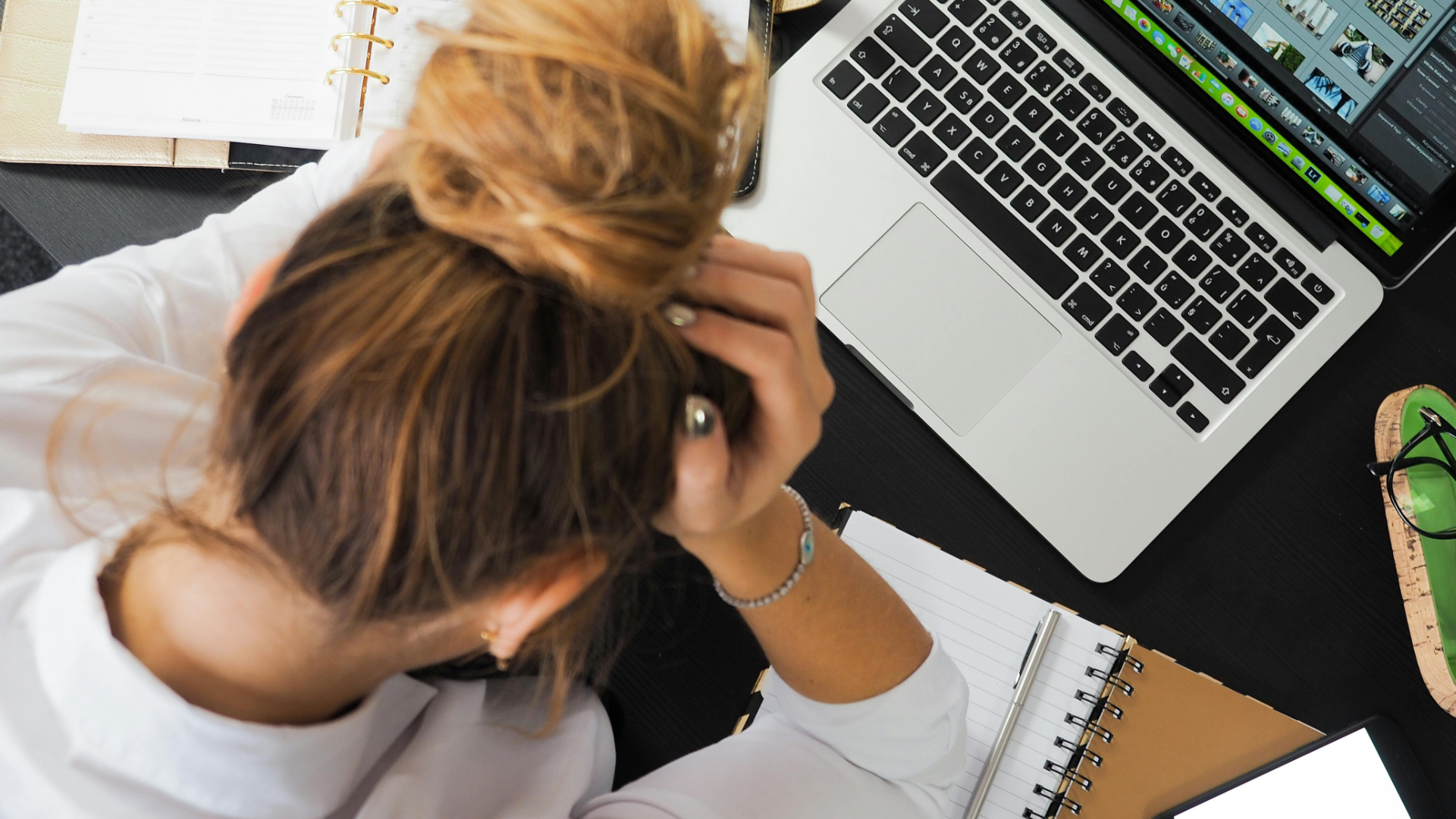Woman with her head in her hands over her desk with her laptop open and papers scattered