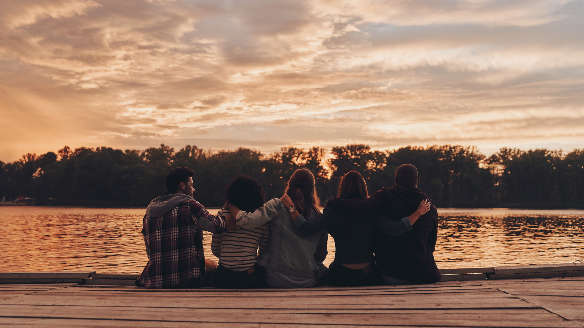 Friends sitting on a dock by the lake at sunset