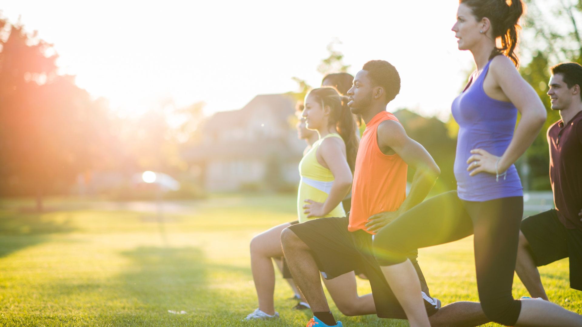Group of people doing leg lunges in park with sun shining